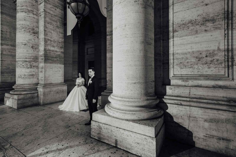 Elegant black and white portrait of a bride and groom at a luxurious historic venue with grand stone columns.