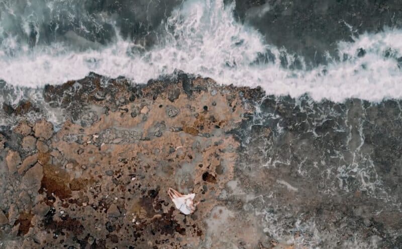 Seaside wedding on rocky coast with ocean waves crashing, romantic couple in white dress, stunning sunset view, high-end luxury wedding venue by the sea, elegant and scenic.