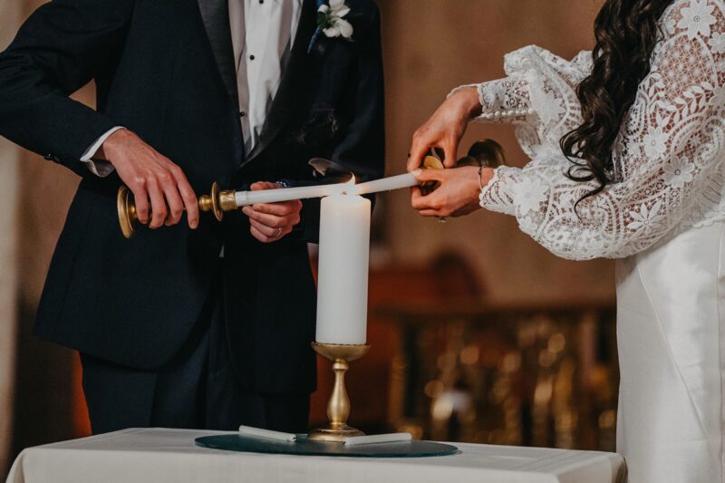 Elegant wedding ceremony with candle lighting, featuring bride in lace gown and groom in tuxedo at luxury venue.