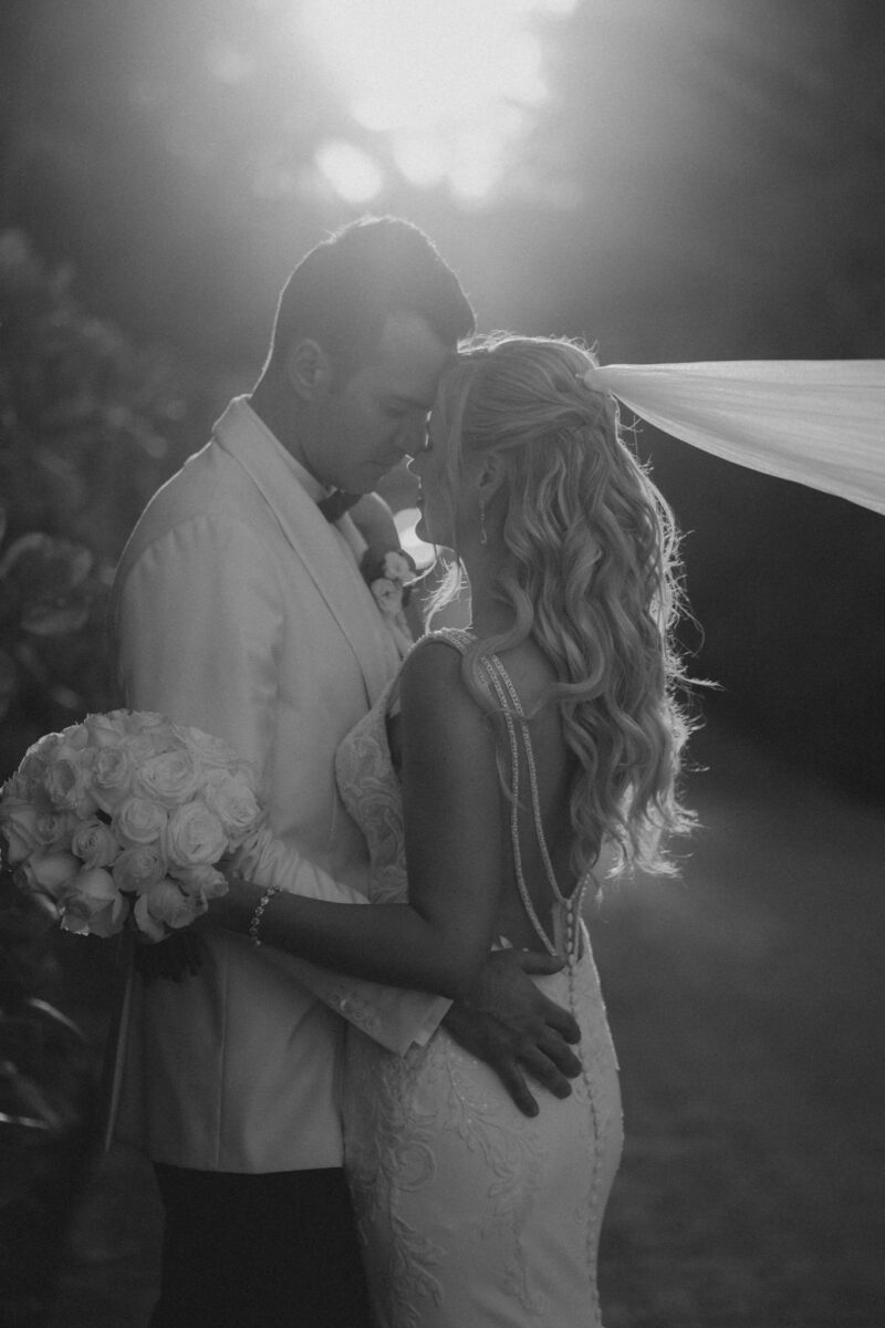 Elegant black and white wedding photo of a bride and groom sharing an intimate moment outdoors at a luxury wedding venue.