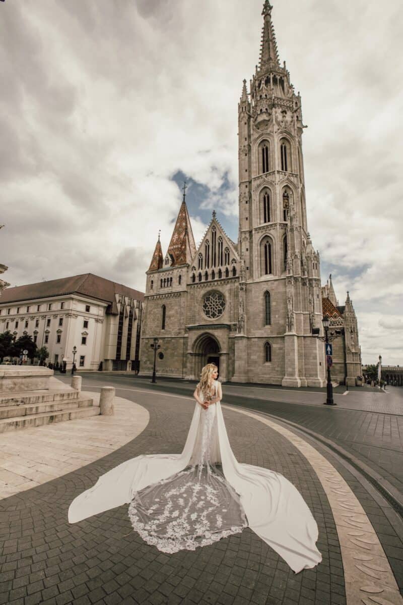 Black and white gothic cathedral wedding venue with a bride in a long lace gown standing on a cobblestone street.