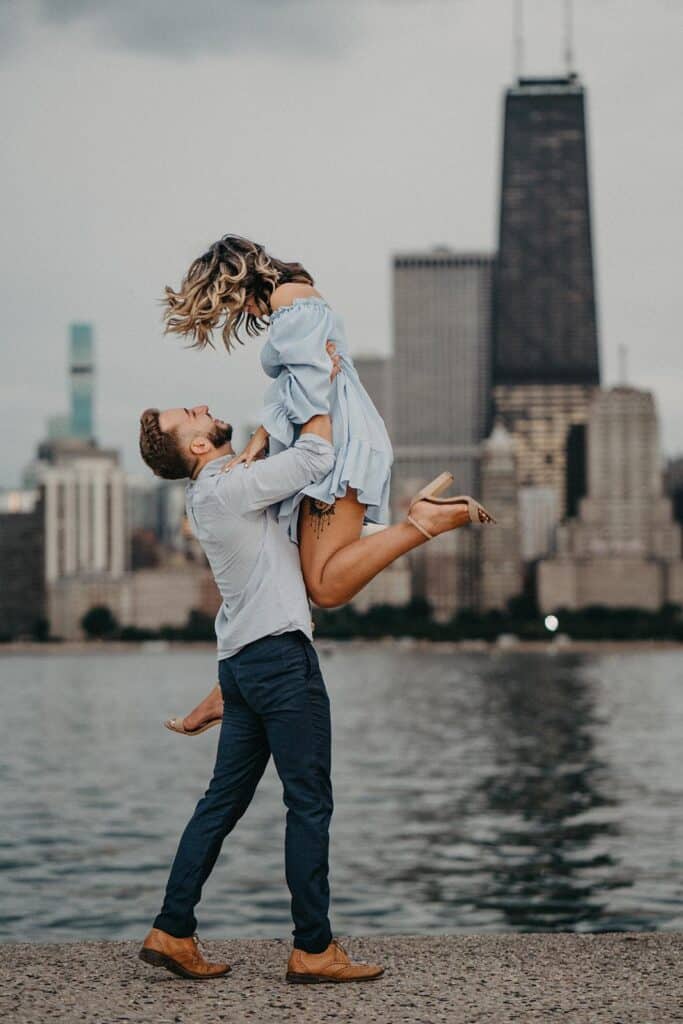 Elegant couple enjoying a romantic moment by the water with a city skyline in the background, perfect for luxury wedding photography.