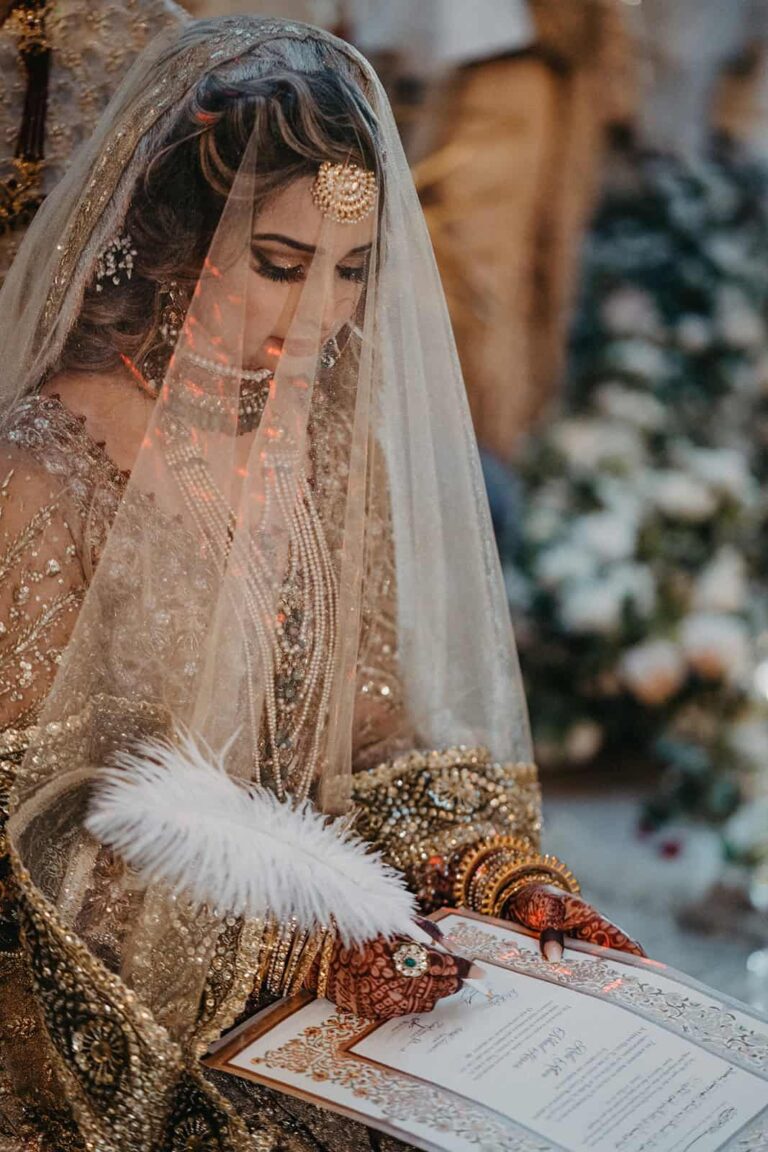 Elegant bride in luxurious traditional wedding attire with intricate jewelry, signing marriage documents at an upscale wedding venue.
