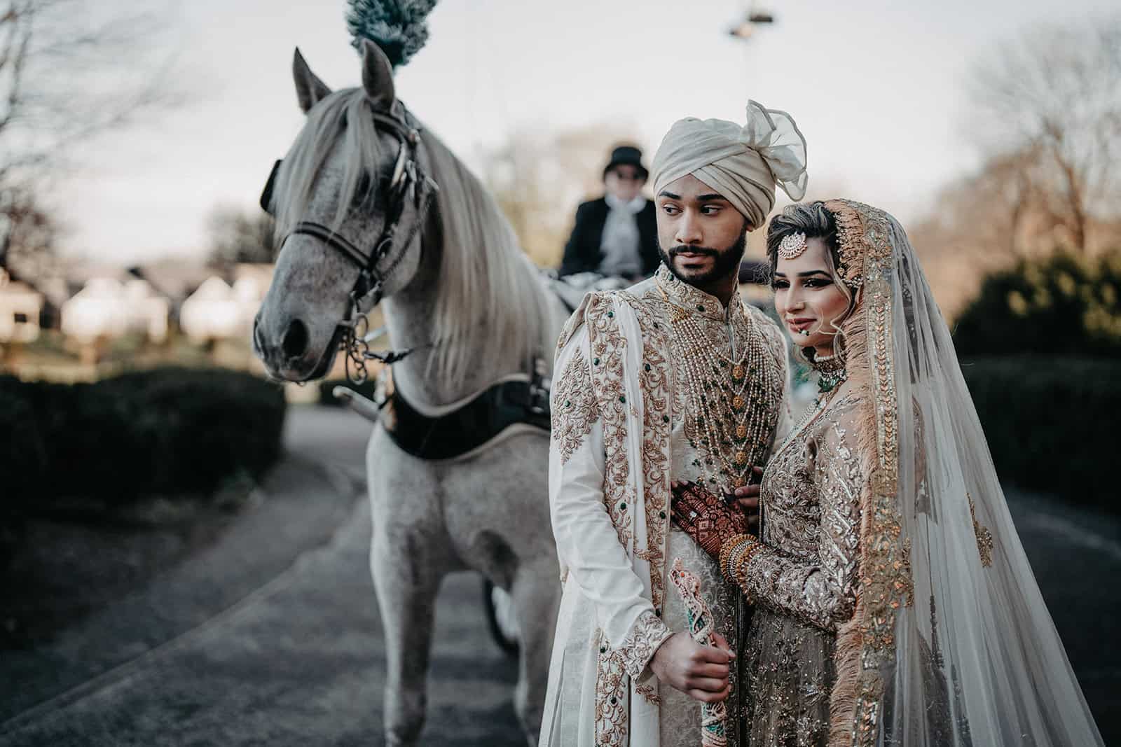 Luxury wedding couple in traditional Indian attire with horse and carriage.