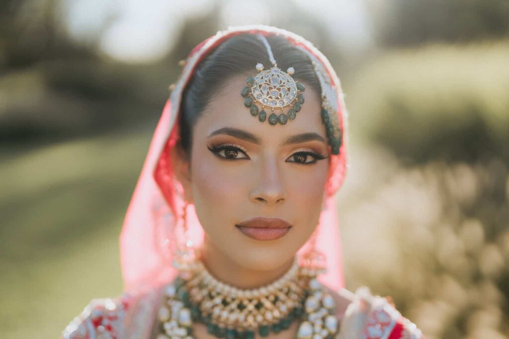 Elegant bridal portrait wearing traditional jewelry and vibrant attire, outdoor setting with soft natural light.