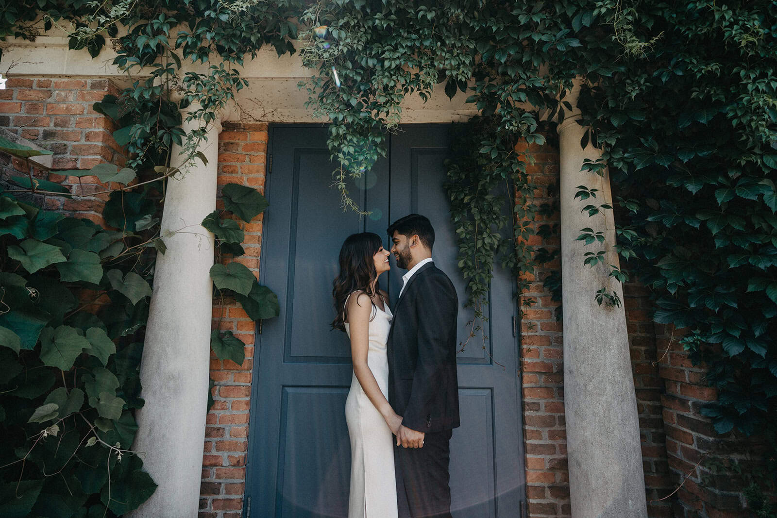 Elegant couple in wedding attire sharing a moment in front of a stylish blue door surrounded by lush green foliage at a luxury wedding venue.