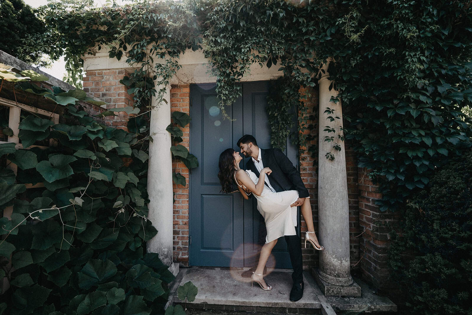 Elegant couple in wedding attire sharing a romantic moment in front of a luxurious, ivy-covered historic villa with classic columns.