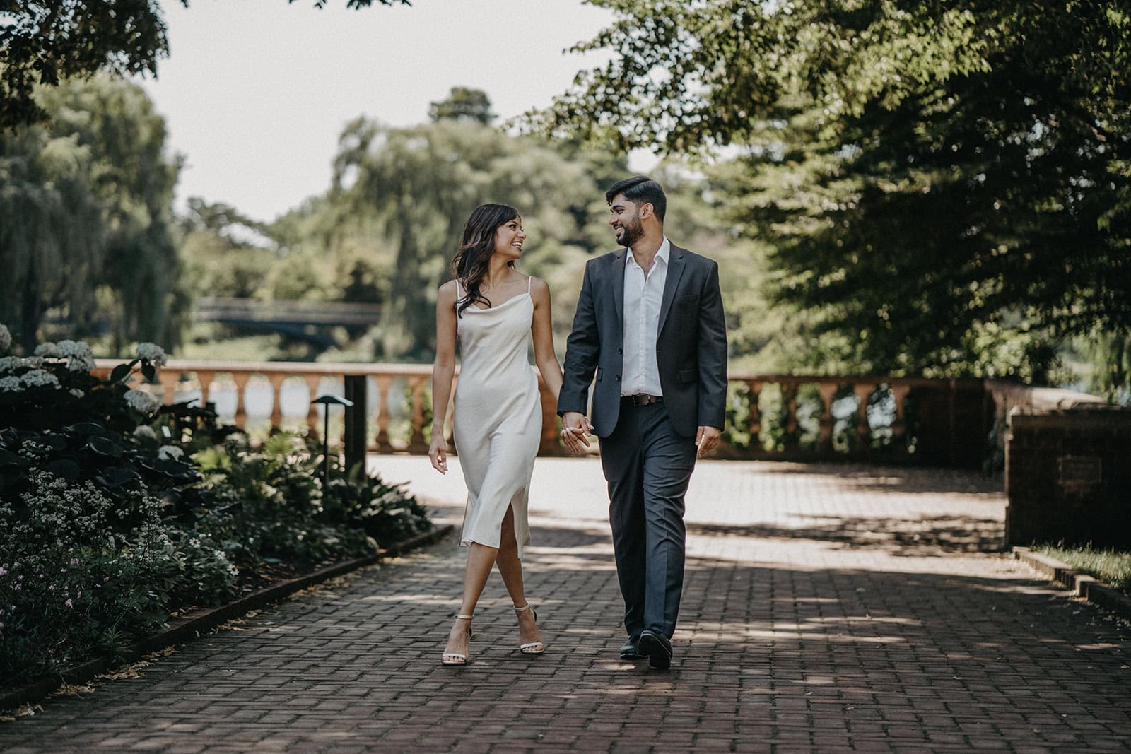Elegant couple walking hand-in-hand in a lush outdoor garden setting for luxury wedding photography.