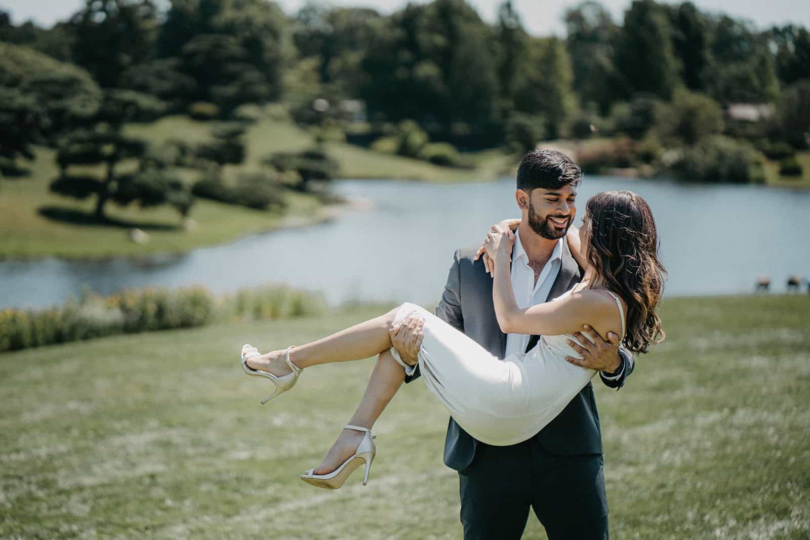Luxury wedding couple outdoors by a scenic pond, elegant attire, romantic moment, high-end venue, wedding photography, picturesque landscape, joyful celebration.