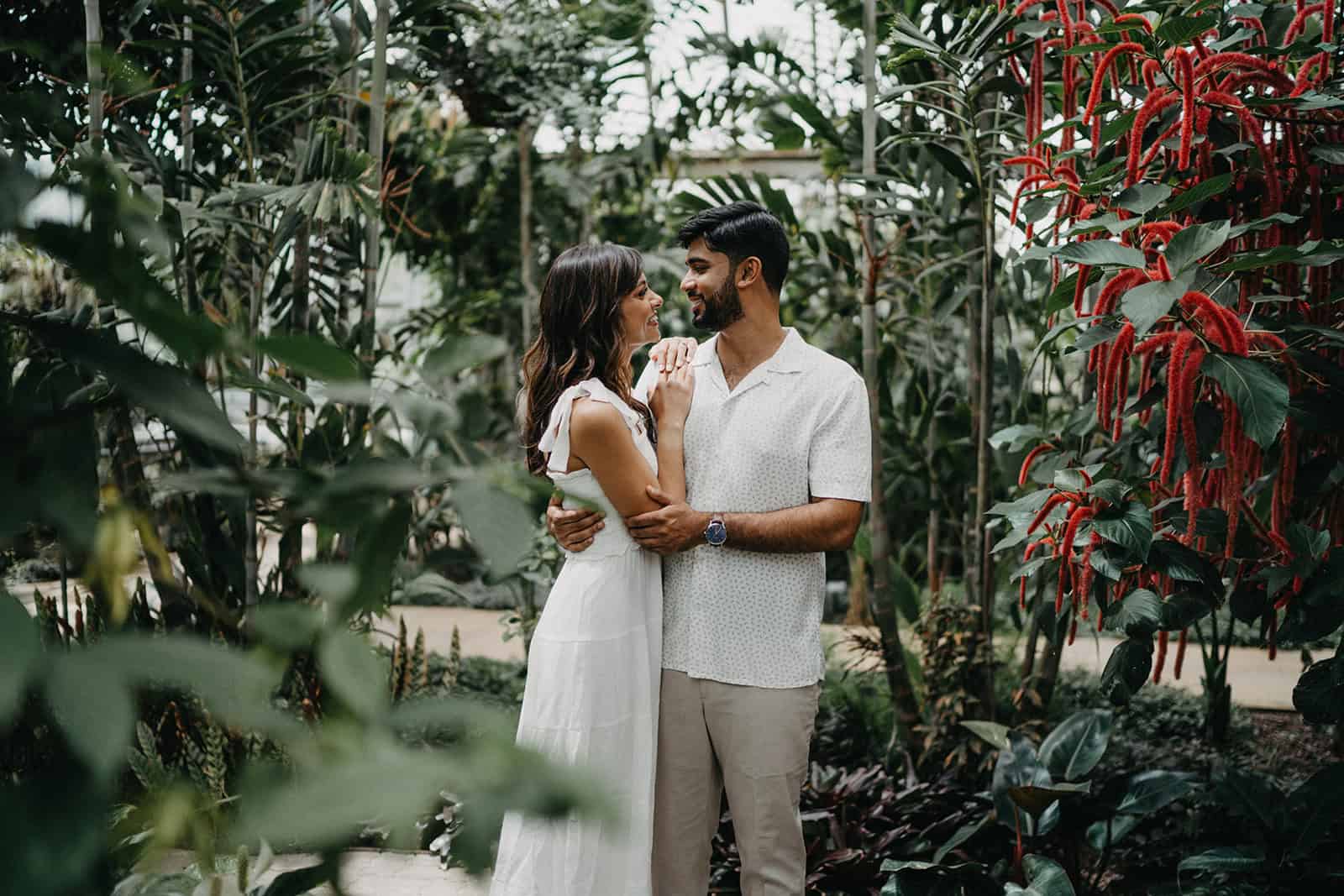 Romantic couple embracing in lush tropical greenhouse setting.