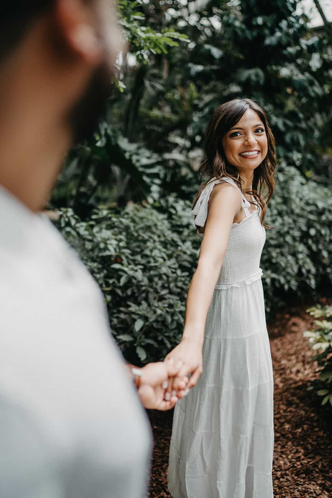 Elegant bride in a white gown holding hands with her partner outdoors at a luxury wedding venue.