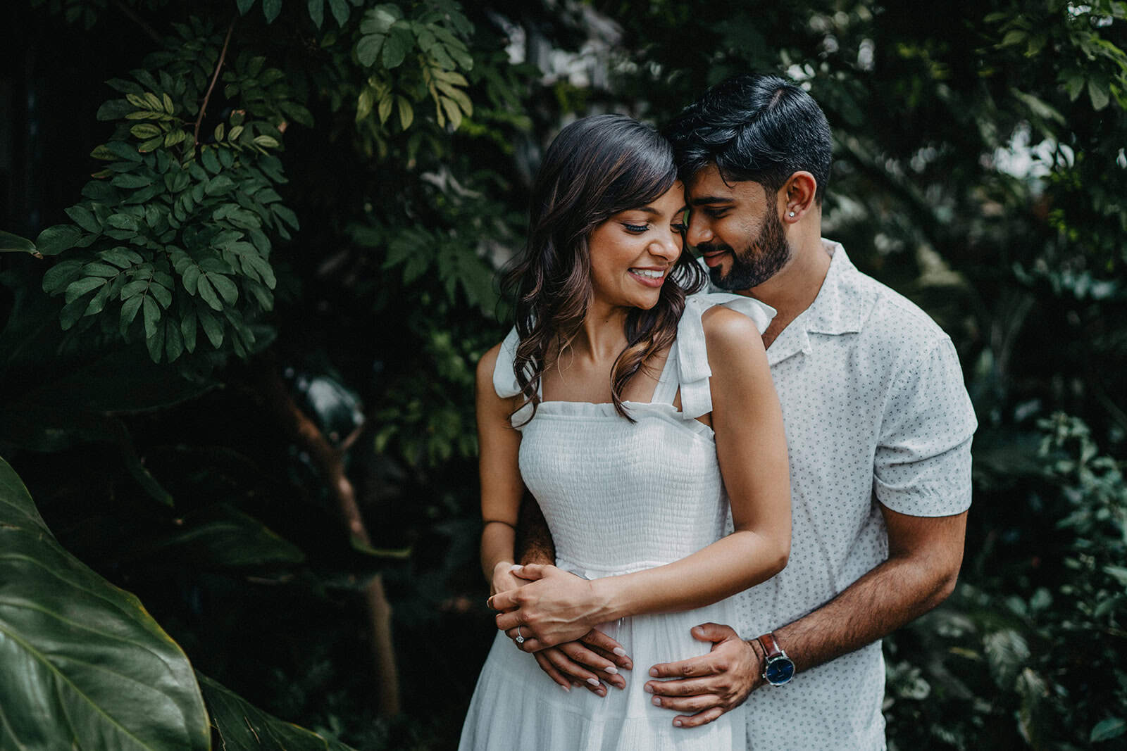 Elegant couple embracing outdoors in lush greenery, showcasing love and intimacy at a luxurious wedding venue.