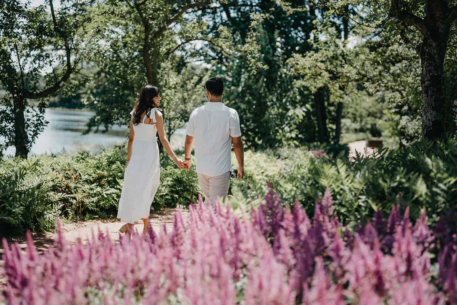 Beautiful couple holding hands walking through lush garden with colorful flowers, romantic engagement scene, outdoor wedding photos, high-end wedding venue setting, elegant romantic ambiance.