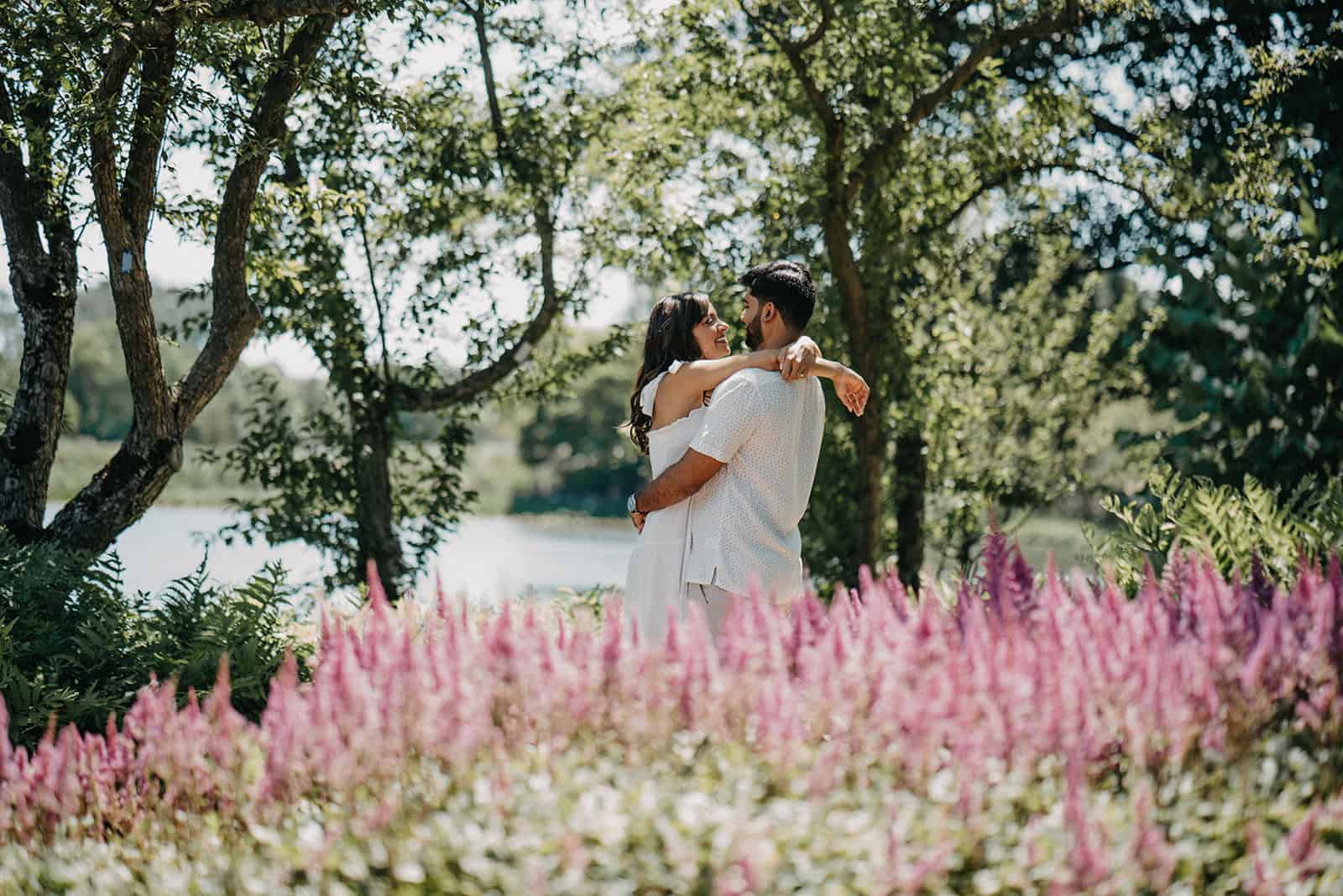 Romantic couple embracing outdoors at a luxurious wedding venue with lush greenery and colorful flowers.