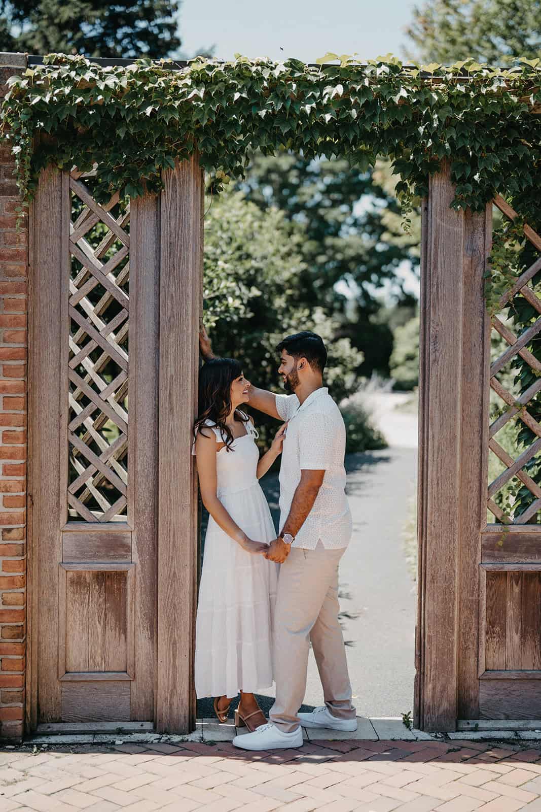 Romantic couple at elegant outdoor wedding venue with lush greenery and wooden gates, perfect for luxury wedding photography and high-end venues.