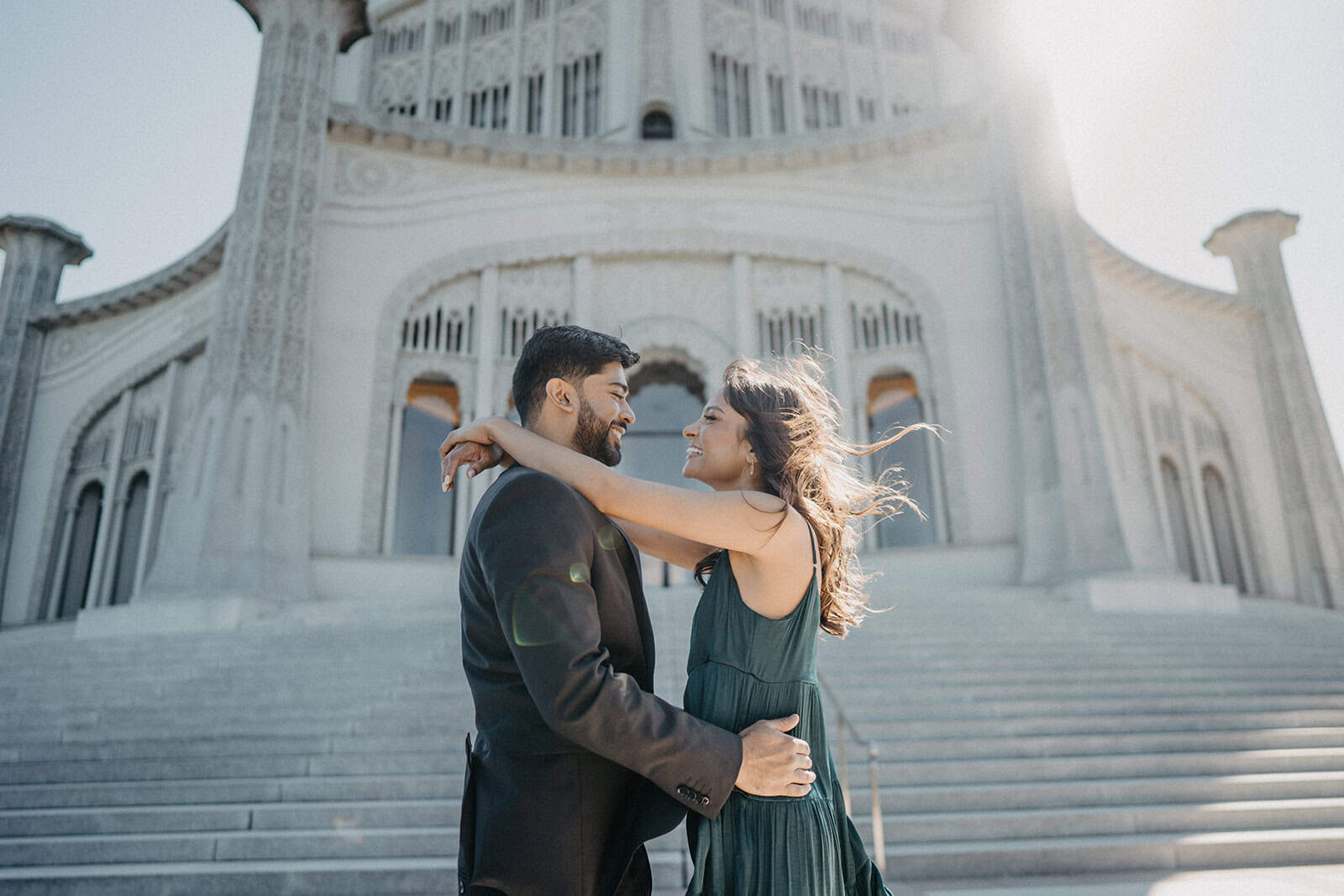 Elegant couple embracing in front of a majestic white wedding venue with grand stairs.