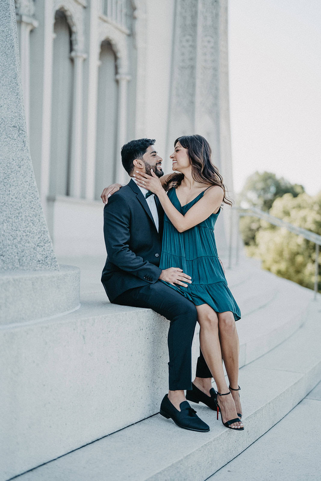 Romantic couple sitting on stairs outside a luxury historic venue, elegant wedding attire, intimate moment, timeless architectural background.