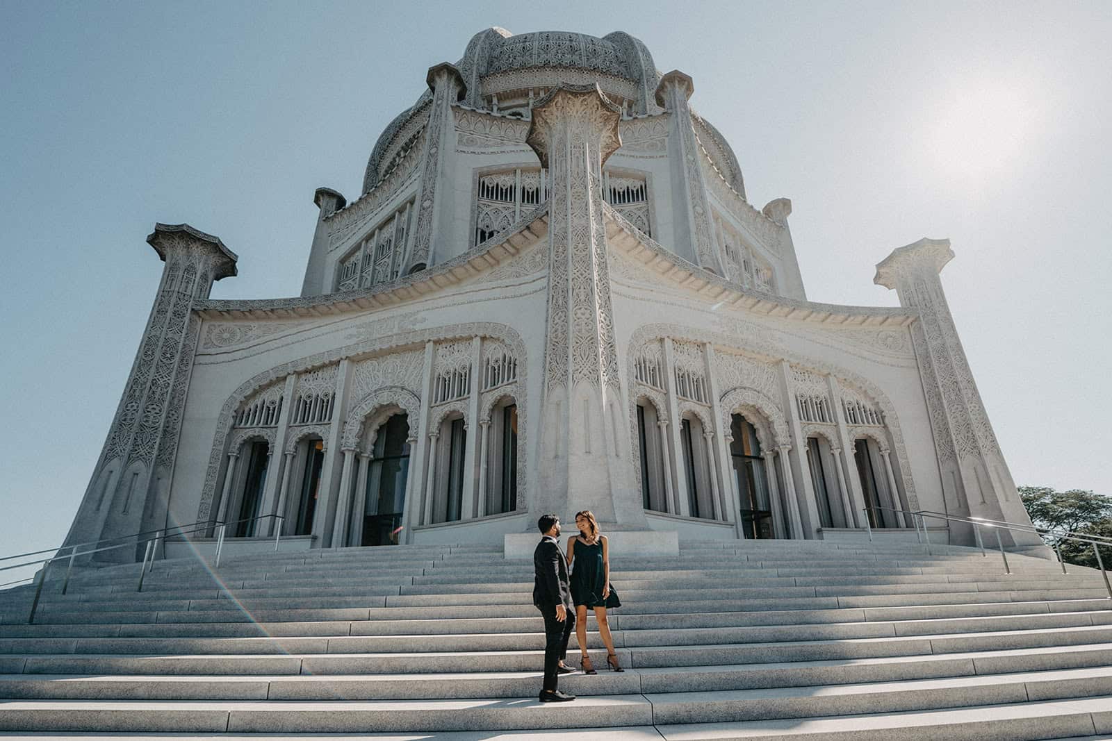 Elegant couple standing on grand staircase in front of ornate white wedding venue, perfect for luxury wedding ceremonies.