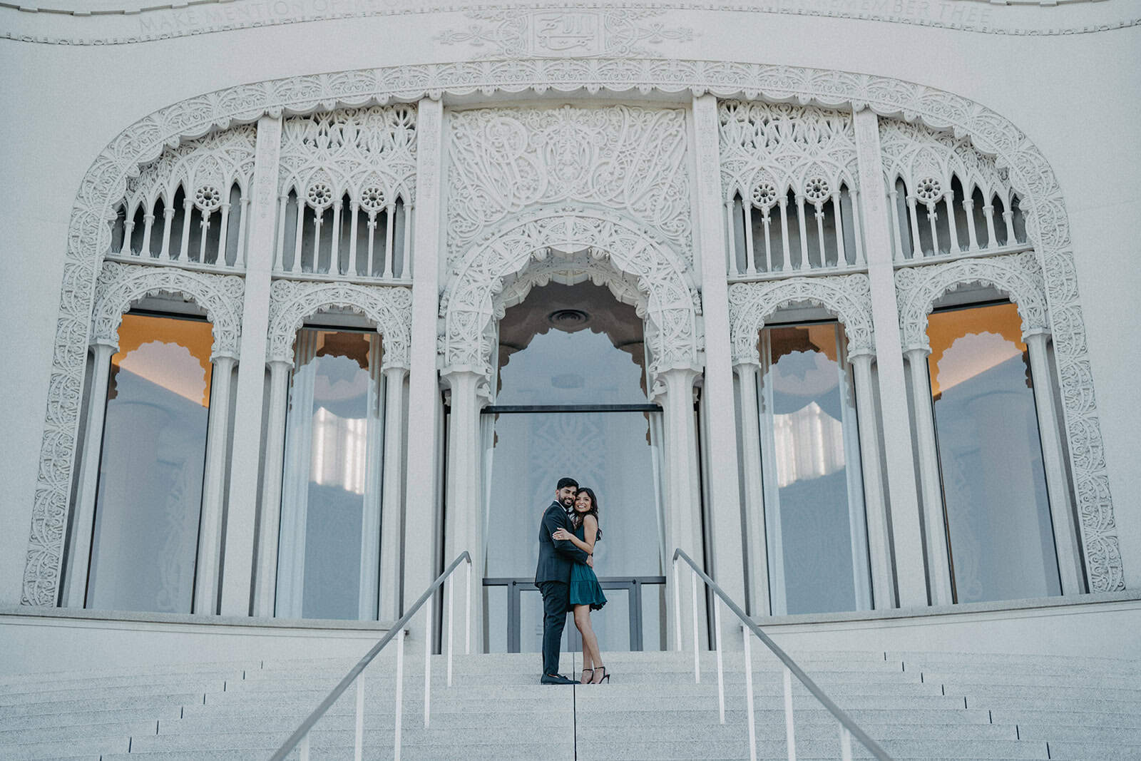 Elegant couple standing in front of ornate white wedding venue with intricate architectural details, perfect for luxury wedding settings.