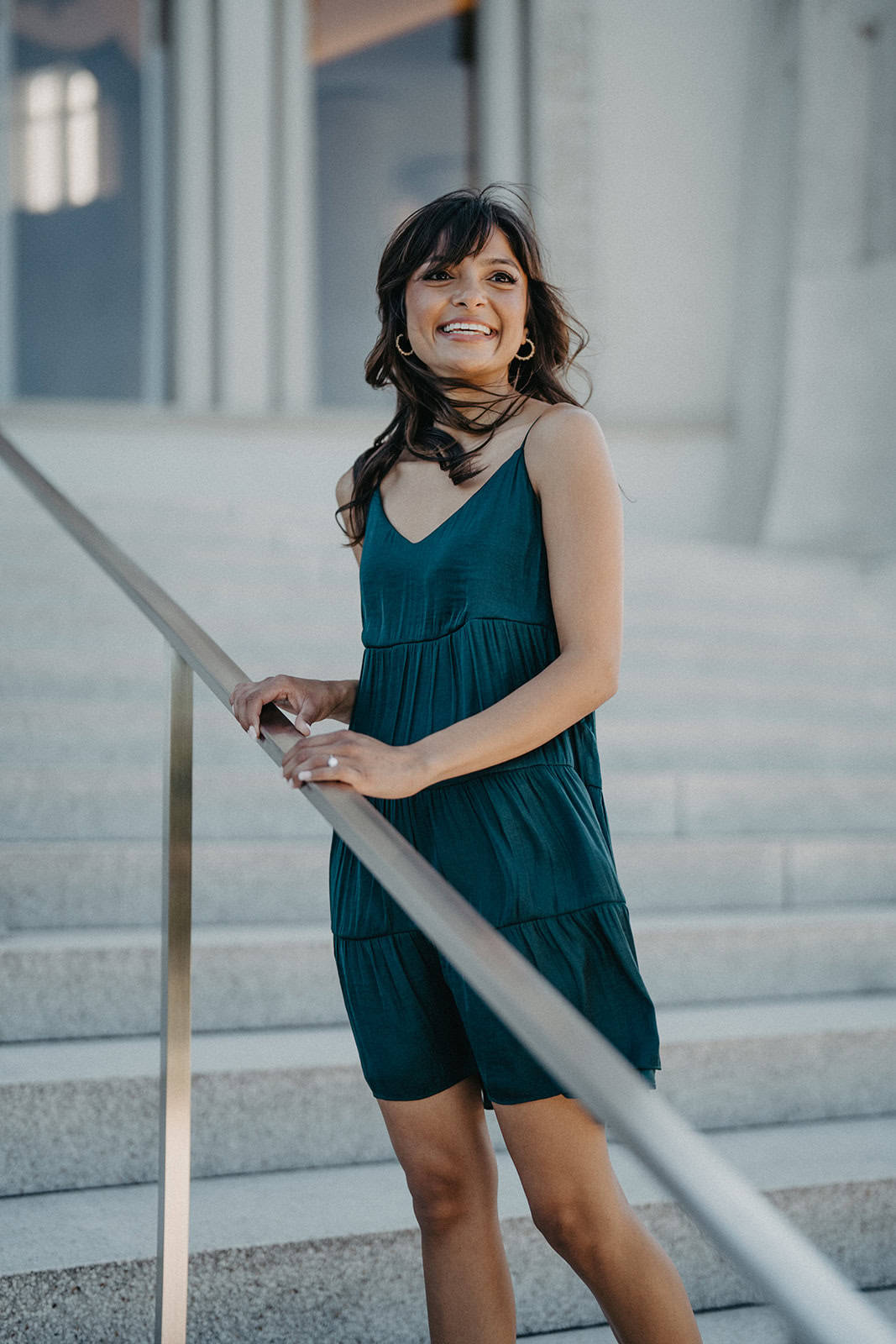 Elegant woman in a teal dress standing outdoors on stairs, beautifully capturing luxury wedding fashion and high-end event style.