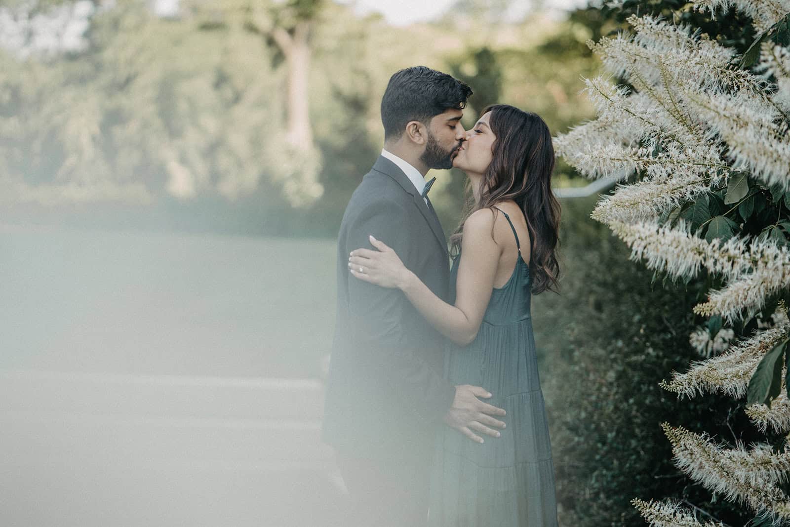 Romantic couple kissing outdoors in a luxurious garden setting, perfect for high-end wedding photography.