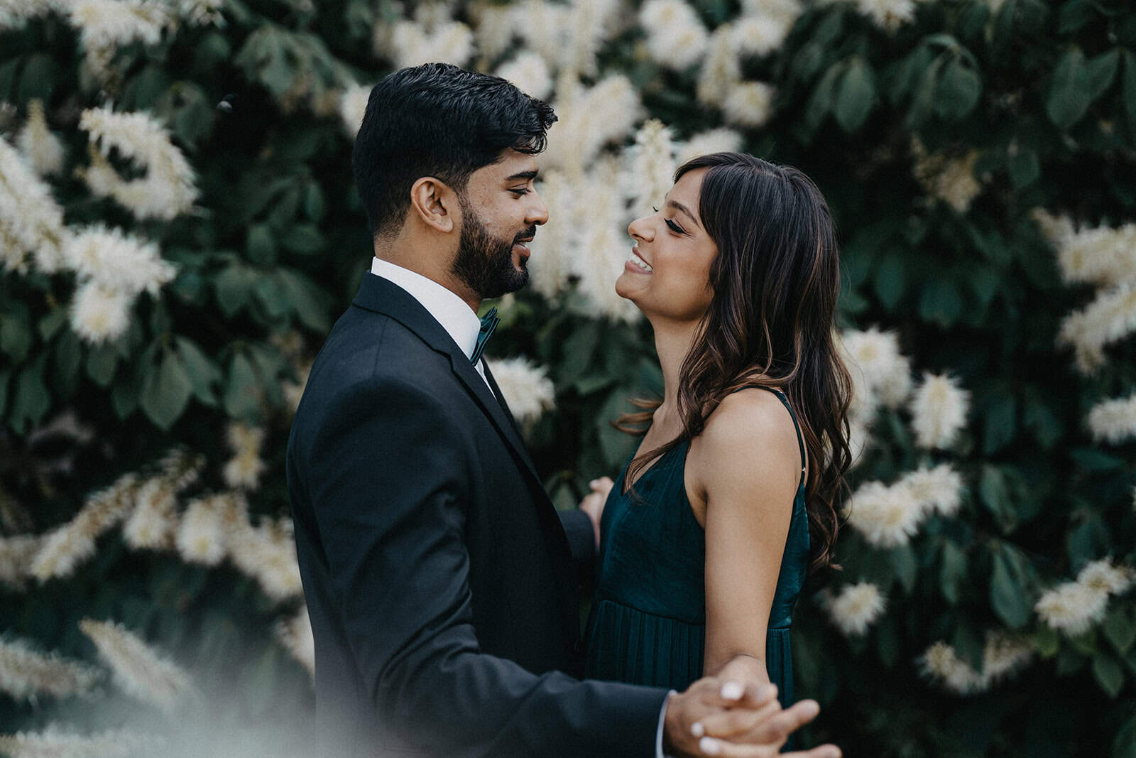 Elegant couple dancing outdoors at a luxury wedding venue with lush greenery and white floral backdrop.