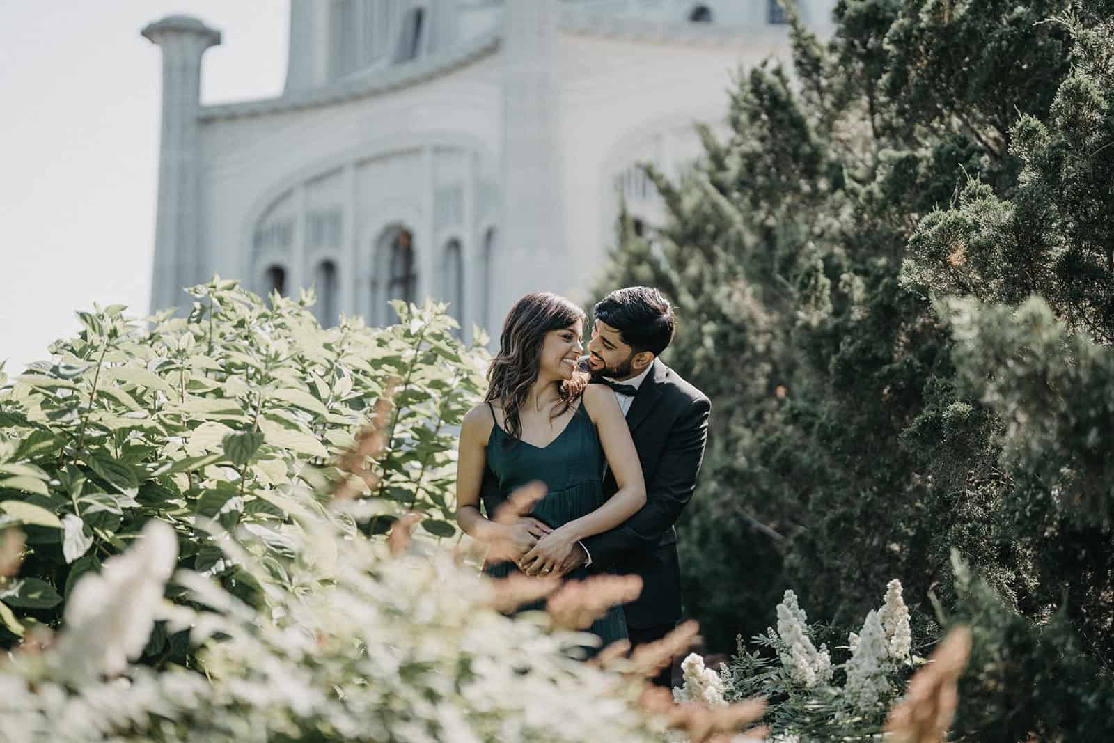 Elegant couple embracing amidst lush greenery at a luxurious outdoor wedding venue.